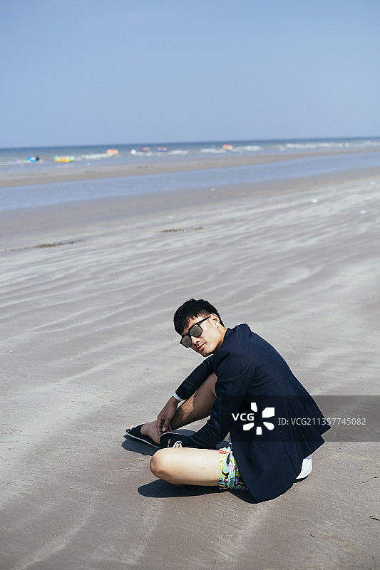 商人戴着太阳镜，下班后坐在海滩上微笑。图片素材