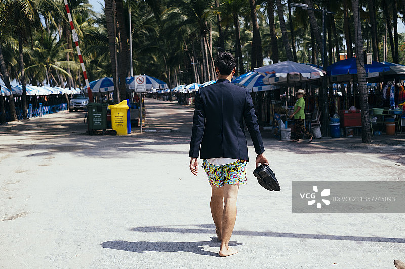 有趣的泰国商人在海滩上赤脚走路，手里拿着鞋子。图片素材