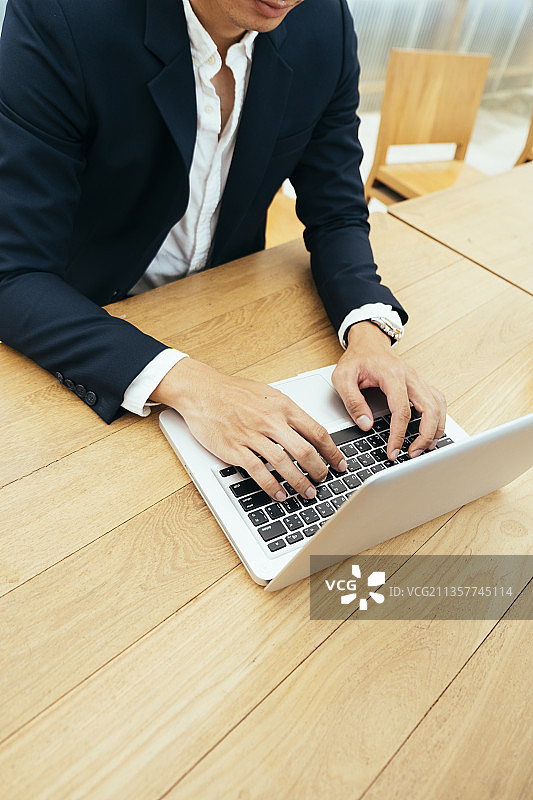 一个商人在木桌上用笔记本电脑工作。图片素材