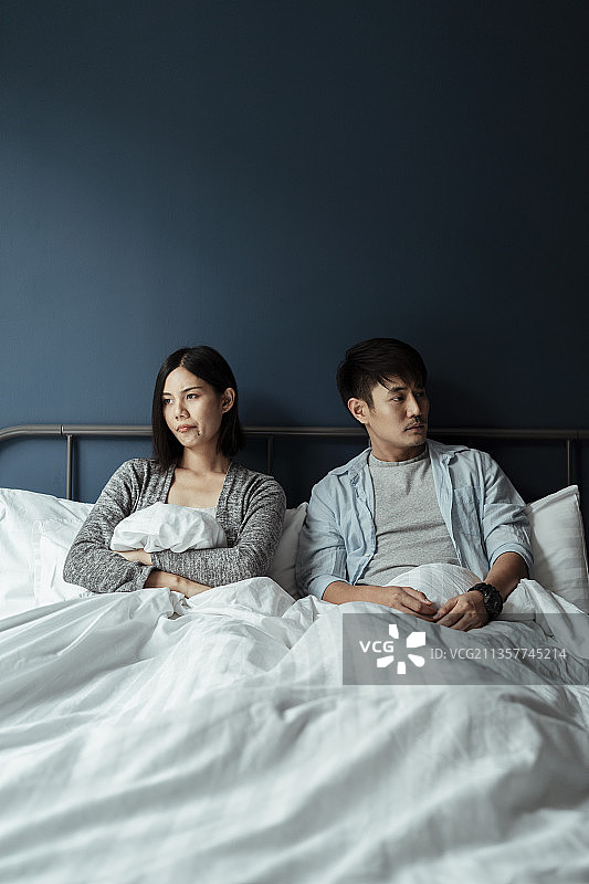 丈夫和妻子坐在白色的床上，但彼此不说话，因为他们很粗暴。图片素材