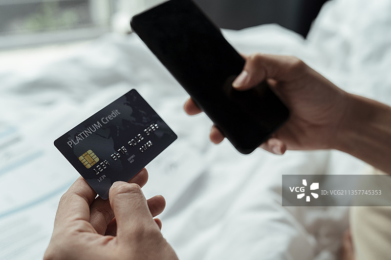 男人手中的信用卡和床上用于网上购物支付的智能手机裁剪图像，水平。图片素材