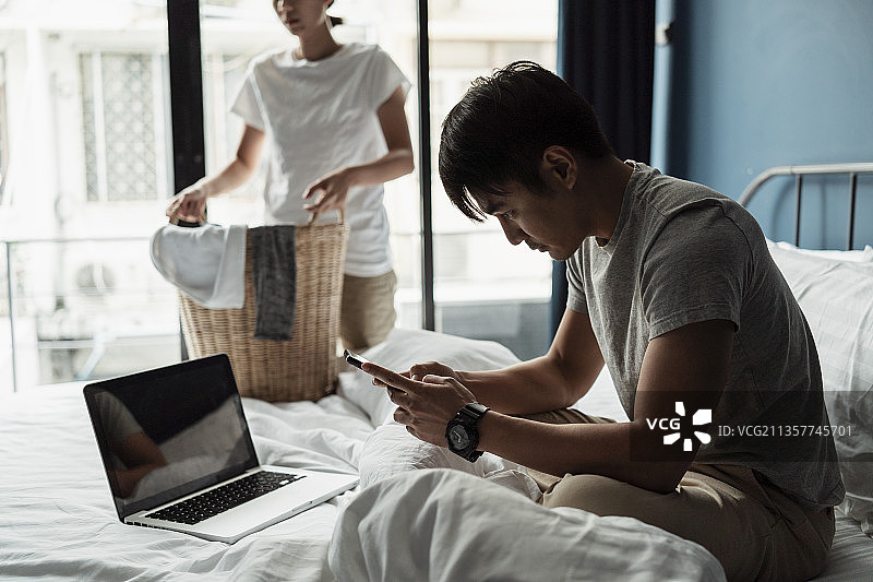 丈夫在看手机，妻子拿着一篮子脏衣服洗。图片素材