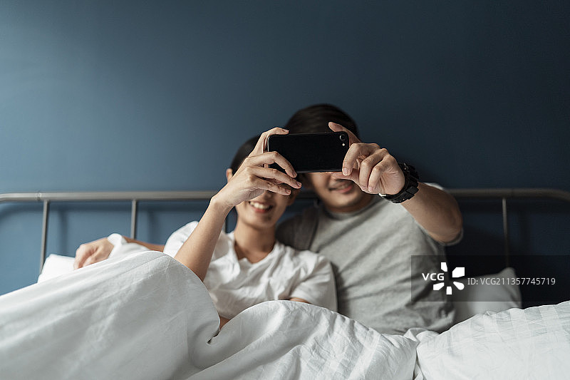 夫妻俩坐在床上，用智能手机一起看电影。图片素材