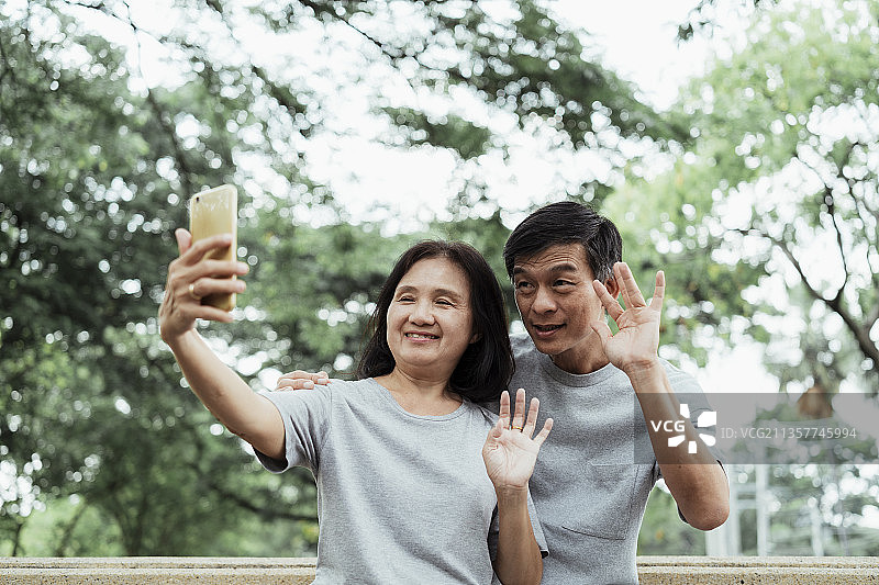 一对老夫妇在绿地公园的桥上给他们的孩子打视频电话。图片素材