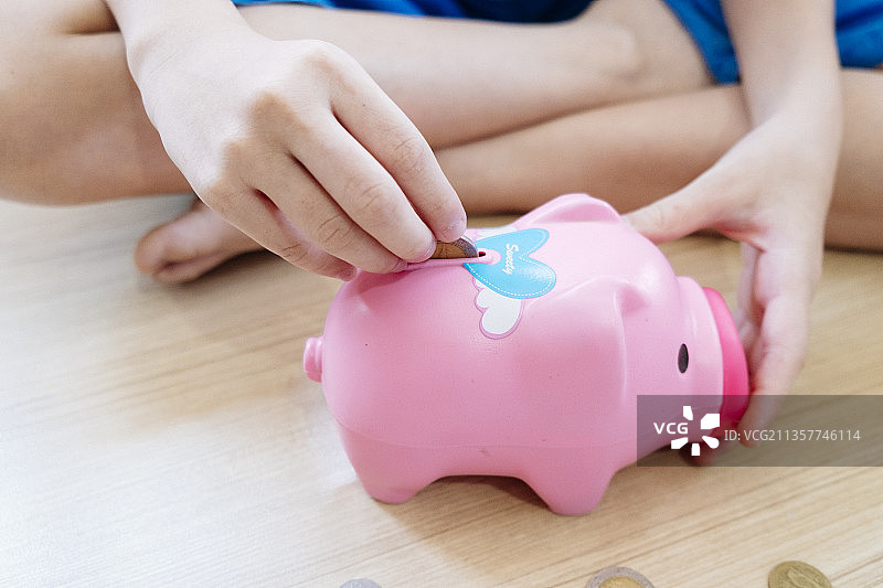 孩子把硬币放进粉红色的小猪储蓄罐。为将来存钱。图片素材