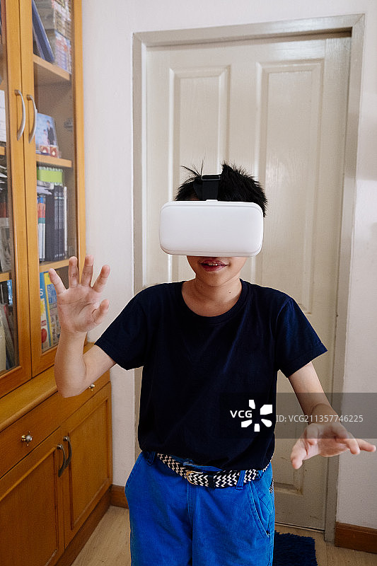 亚洲男孩戴着3D VR眼镜在家里客厅玩游戏。图片素材