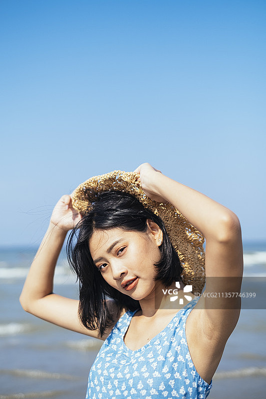 可爱的黑发女孩在阳光下拿着她的帽子在海上。图片素材