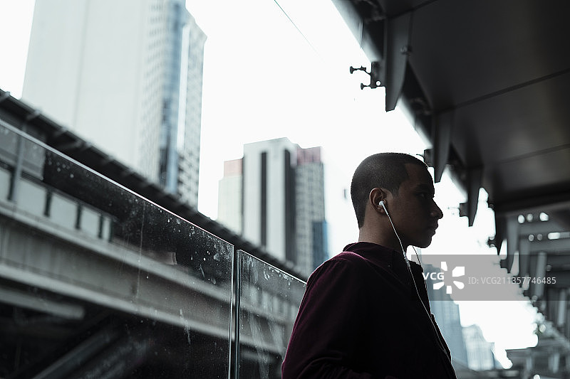 穿着红衬衫的光头党倚着玻璃路障，用耳机听着音乐。图片素材