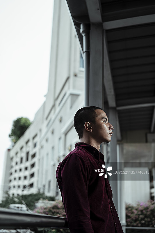 穿着红衬衫的光头党男子在清晨空荡的头脑中靠在人行道的扶手上。图片素材