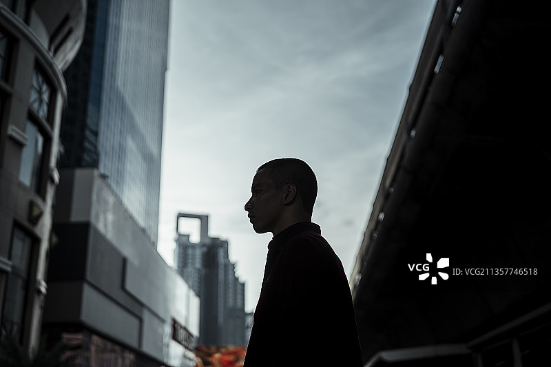 光头男站在城市道路上方的天桥上的剪影。图片素材