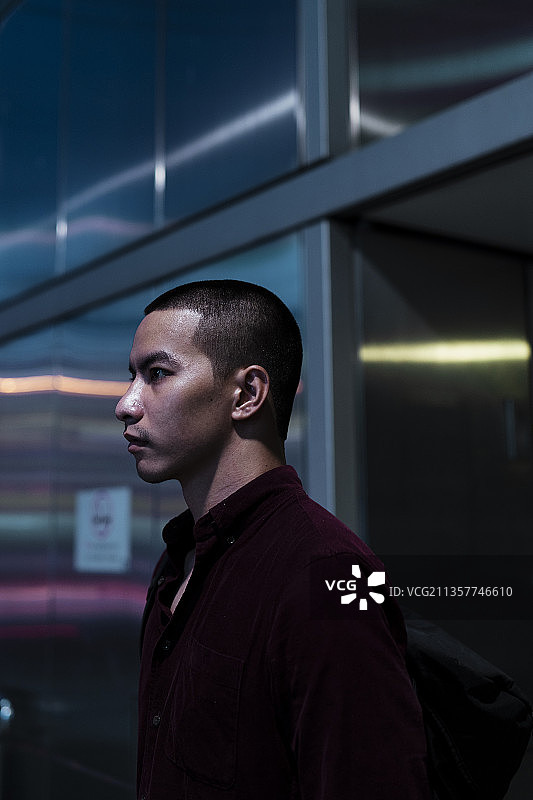 在城市的夜晚，穿着红衬衫的光头党站在金属建筑前。图片素材