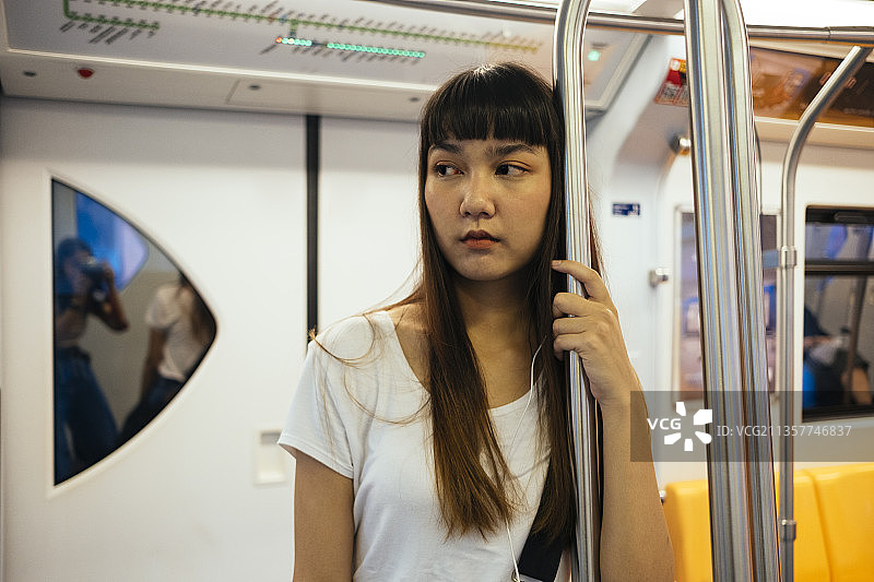 可爱的泰国年轻女子刘海发型抓杆，听音乐耳机，站在火车上。图片素材