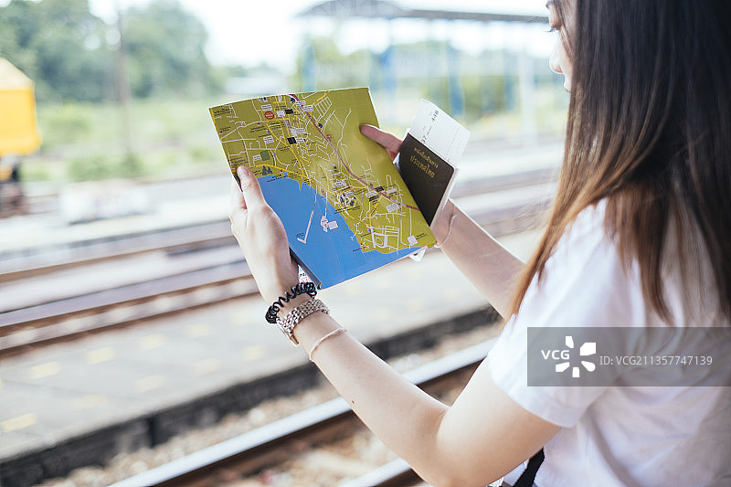 年轻的亚洲人泰国长黑发旅行者妇女阅读地图和泰国护照在火车站。图片素材