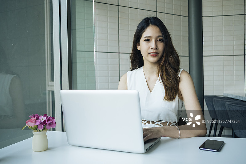 年轻的泰国妇女使用笔记本电脑在现代办公室工作。漂亮的办公室女职员用笔记本电脑工作。图片素材