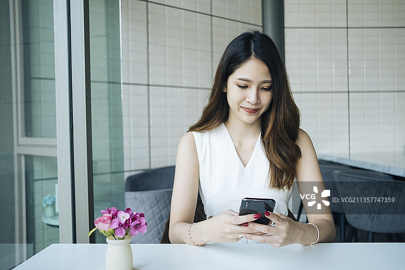 穿着白衬衫的亚洲女性正在用智能手机和朋友聊天。图片素材