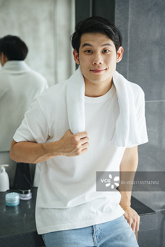 亚洲年轻男子在浴室洗澡后，身穿白衬衫，手拿毛巾。图片素材