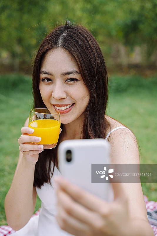 美丽的亚洲旅行者女人的肖像与橙汁自拍照。图片素材