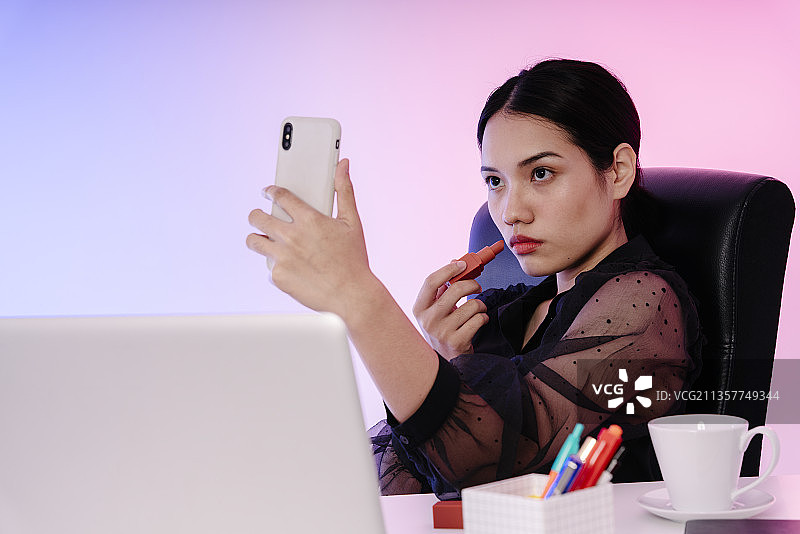 亚洲女商人在办公室工作时涂口红。图片素材