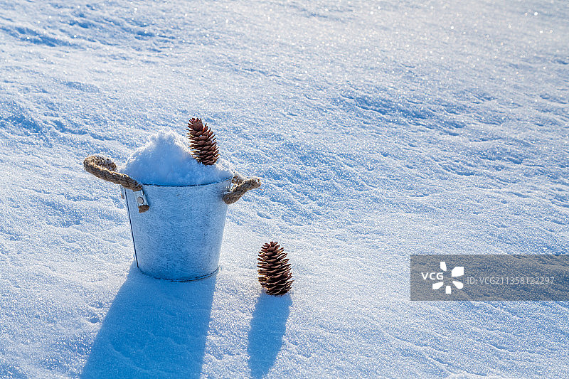 雪地上装满雪的小桶，松枝和松果图片素材