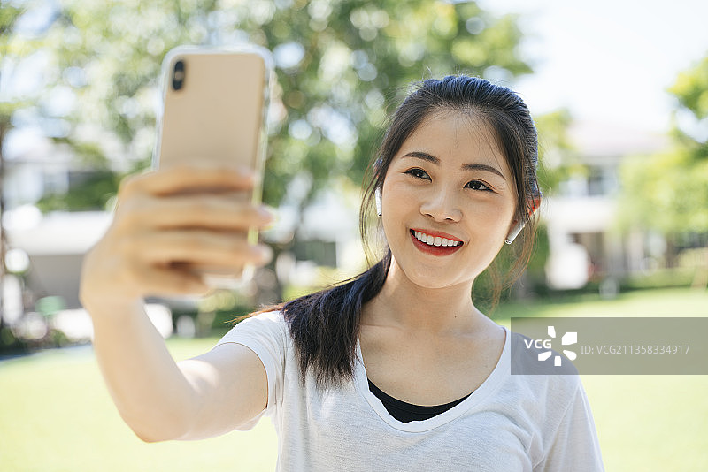 运动的亚洲女性在公园用智能手机发关于运动的视频或自拍。图片素材