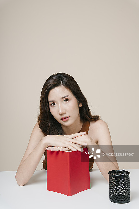 一个年轻漂亮的亚洲女人的肖像，在办公室桌子上有一本红色的书。图片素材