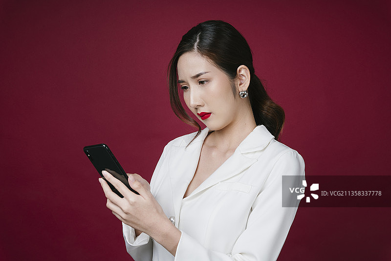 美丽的年轻亚洲女人在白色夹克西装肖像使用智能手机为化妆品购物。图片素材