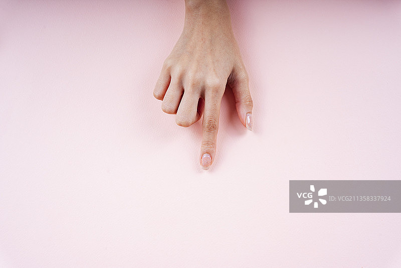 女人用手指着粉红色背景上的空白区域。图片素材