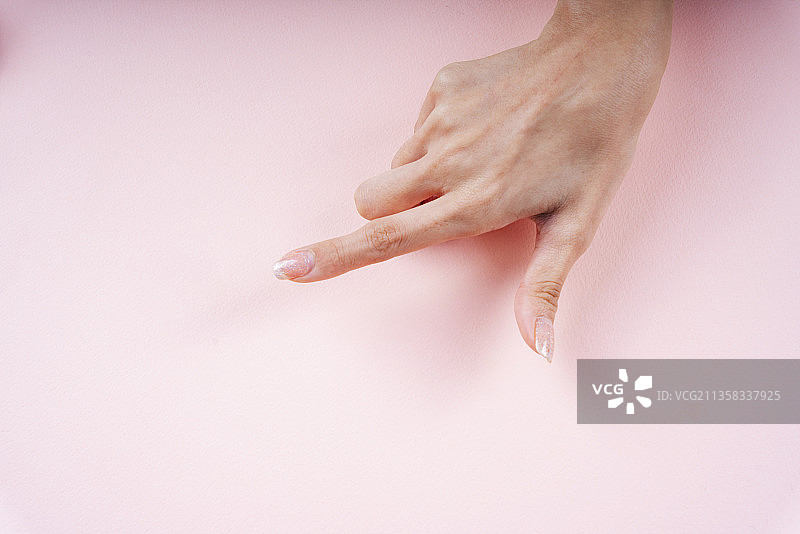 女人用手指着粉红色背景上的空白区域。图片素材