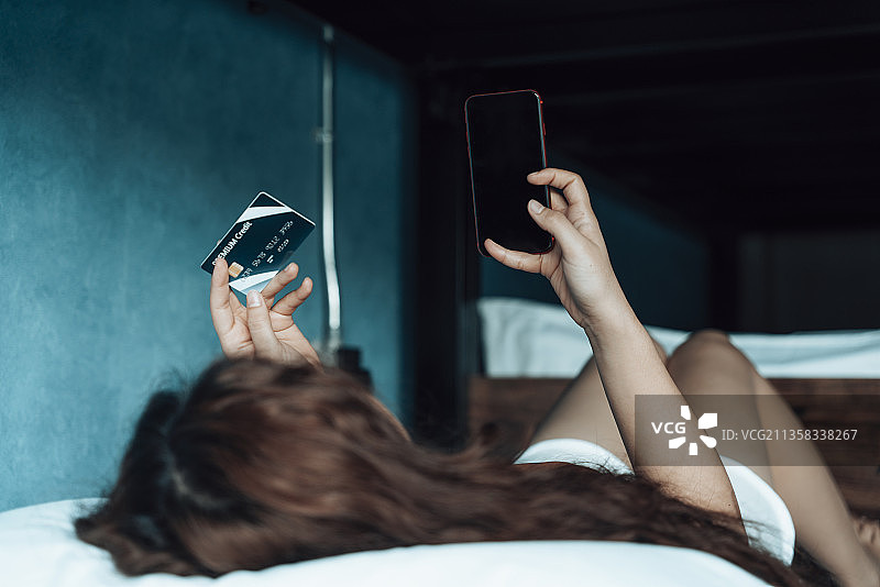 女人躺在床上使用信用卡网上购物与智能手机应用程序。图片素材