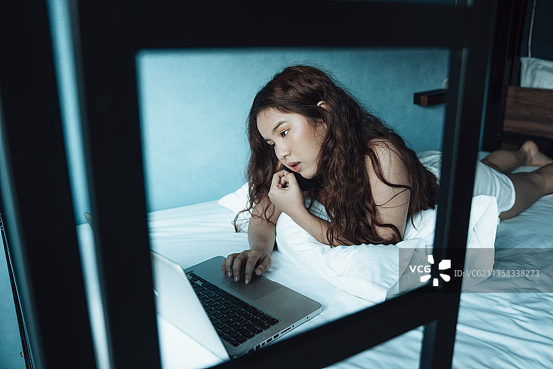 一个大学生在校园宿舍边做作业边和她的朋友聊天。图片素材