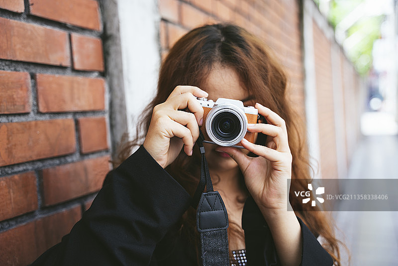 时尚肖像年轻亚洲妇女穿着黑色夹克拍照与相机。图片素材