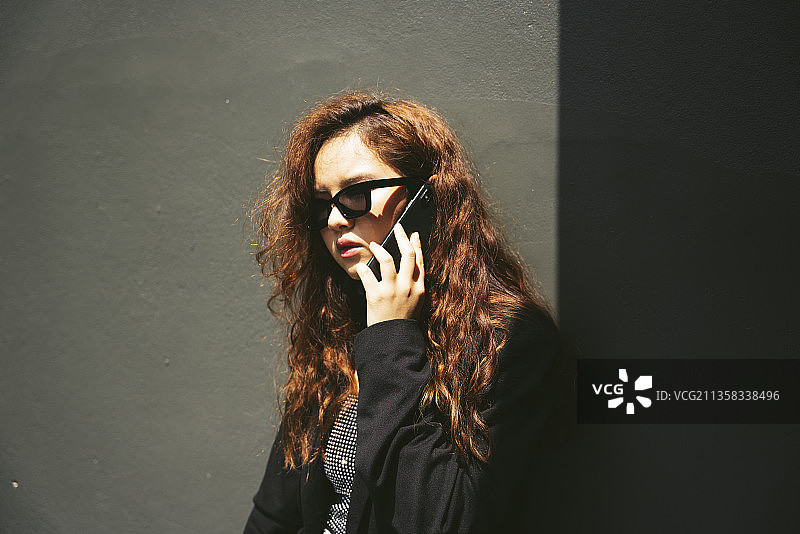 年轻的亚洲女性戴着太阳镜，穿着黑色夹克，使用智能手机的时尚肖像。图片素材
