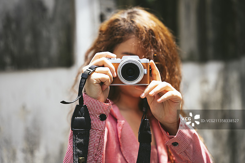 近距离肖像年轻亚洲妇女持有小型相机在街上。图片素材