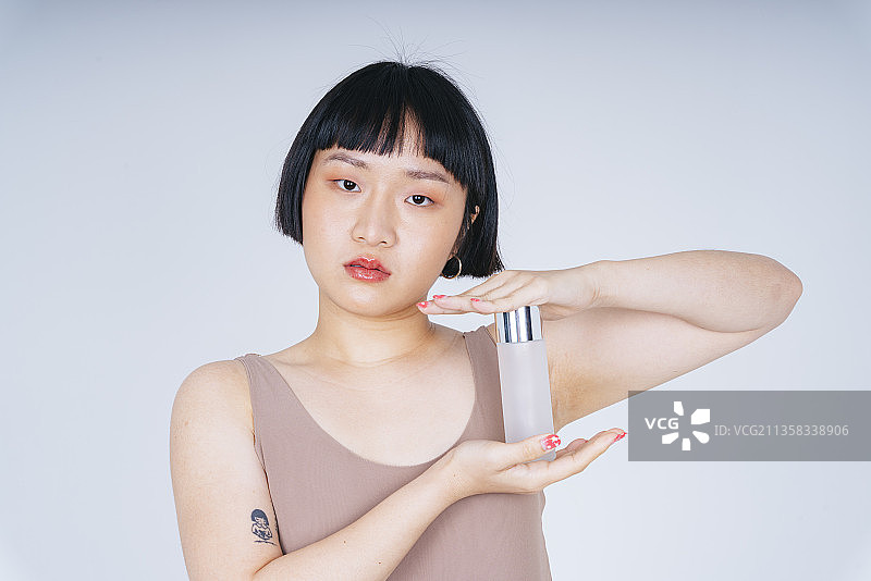 年轻的亚洲短发发型女人手持乳液或香水瓶的特写分离在白色背景上。图片素材