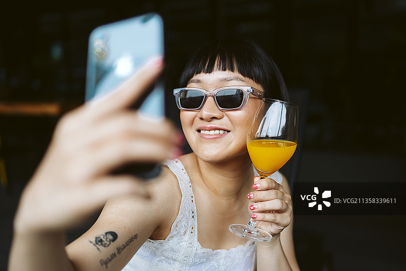 亚洲短发女人戴着墨镜与橙汁自拍。图片素材