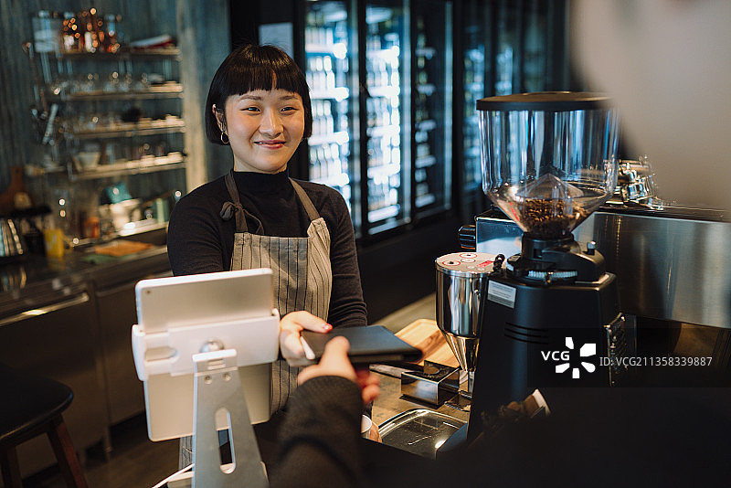 亚洲短发女咖啡师给顾客二维码支付账单。图片素材
