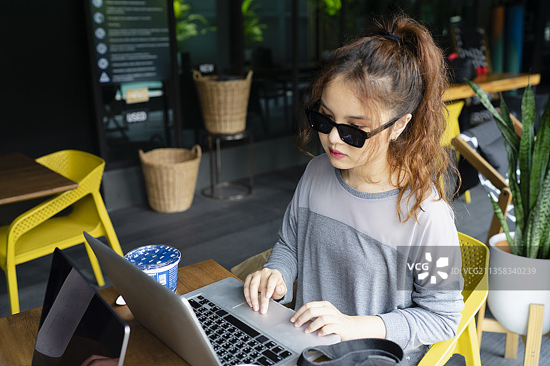 美丽的亚洲女人戴着太阳镜工作在咖啡馆户外笔记本电脑。图片素材