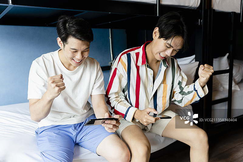 亚洲大学生在宿舍玩手机游戏。两人都赢了比赛。图片素材