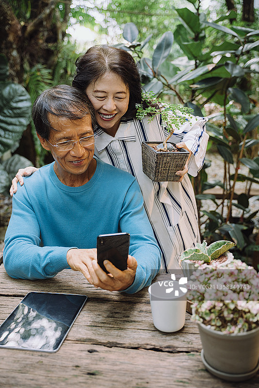 开朗的亚洲老夫妇在公园用智能手机自拍。图片素材