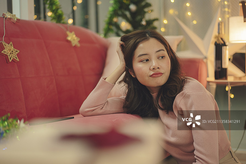 美丽年轻的亚洲女人黑发抓她的头独自坐在客厅。图片素材