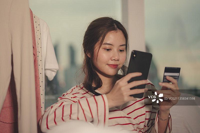 美丽年轻的亚洲女人黑发网上购物智能手机与信用卡。图片素材