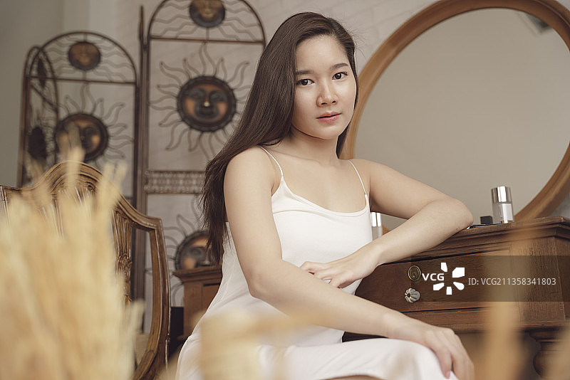 年轻的亚洲美女在白衣坐在化妆台。图片素材