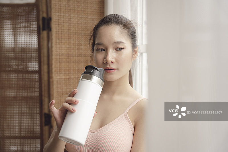 健康的年轻亚洲女性锻炼后休息，喝瓶装水。图片素材
