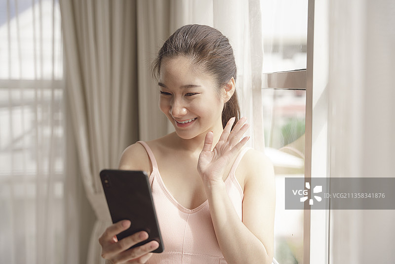 年轻的亚洲美女使用智能手机做视频或在家直播。图片素材