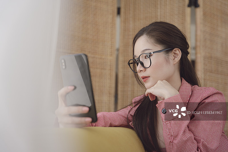 侧视图-年轻的亚洲美女戴眼镜的视频或直播与智能手机。图片素材