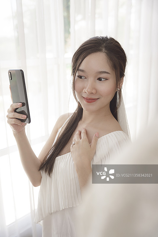 穿着婚纱的新娘在展示厅里用智能手机自拍。图片素材