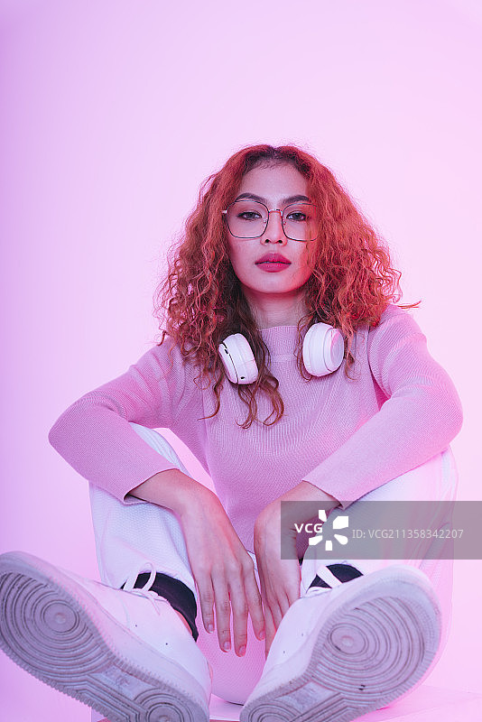 亚洲年轻美女卷发女孩与无线耳机在霓虹灯演播室。图片素材