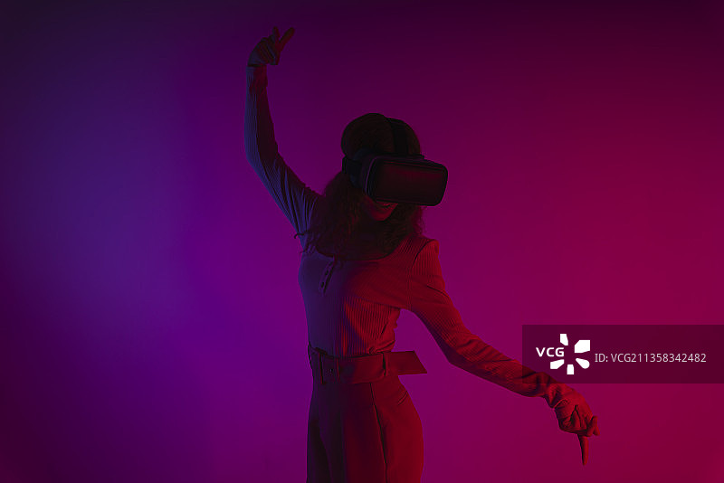 快乐女人在霓虹灯背景下戴着虚拟现实VR眼镜。图片素材