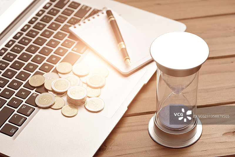 放在笔记本电脑上的办公用品、钱币和沙漏图片素材