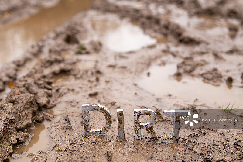 潮湿粘土表面上由银色金属字母组成的“污垢”字样图片素材